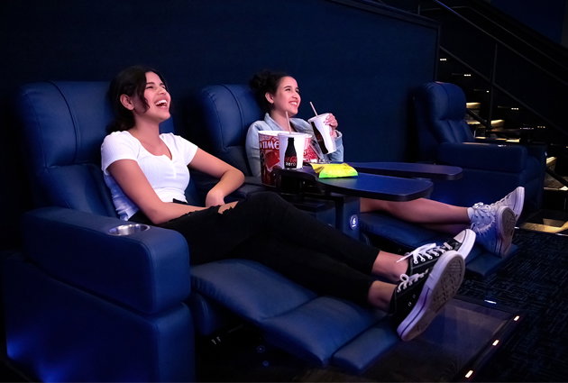 Two Women Sitting in Reclined Seats With Concessions Items